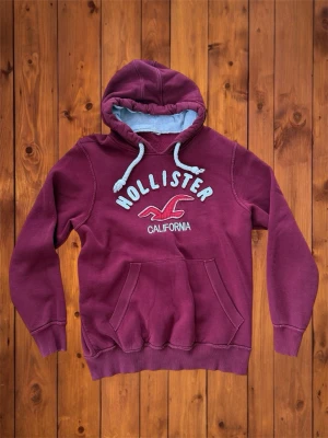 Vintage Hollister hoodie (sällsynt) - Säljer denna vintage, sällsynta och asfeta hoodien från Hollister. Den är riktigt fet och har snygg design på framsidan. Det är en unik vinröd färg som gör vintage känslan ännu starkare. Storlek är M och den passar som M. B=70cm A=57cm