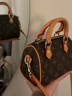 Louis Vuitton💖 - Säljer en brun handväska från Louis Vuitton med klassiskt monogrammönster. Väskan har beige läderhandtag och detaljer, samt guldfärgade metalldelar. 