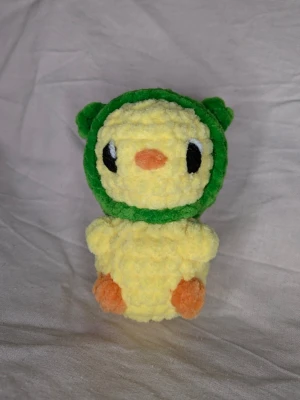 Anka med en grodahatt🐸 - Söt handvirkad gosedjur i mjukt garn. Ankan är gul och har en grodahatt. Den är 11 cm hög och 7 cm bred. Perfekt som dekoration eller present till någon som gillar unika mjukisdjur.