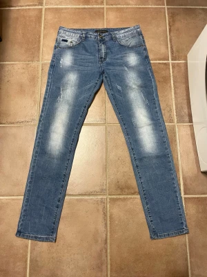 Blå slitna jeans med raka ben - Snygga blå jeans med raka ben och slitna detaljer på både fram- och baksida. Jeansen har klassisk femficksdesign och ljusa partier för en trendig look. Perfekta för dig som gillar en avslappnad och modern stil.
