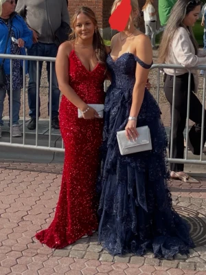 Röd glittrig långklänning med öppen rygg - Säljer min röda balklänning. Det är en röd långklänning med djup v-ringning med knytning i ryggen. Klänningen har ett längre släpp baktill. Perfekt för bal eller speciella tillfällen. Använd en gång ❤️jag är 155 cm lång. 