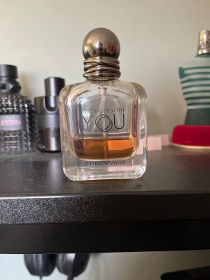 Emporio Armani Stronger With You parfym - Emporio Armani Stronger With You är en elegant parfym i en genomskinlig glasflaska med rundade former och silverfärgad metallkork. Doften har en varm bärnstensfärgad vätska och flaskan har stilren logotyp framtill.