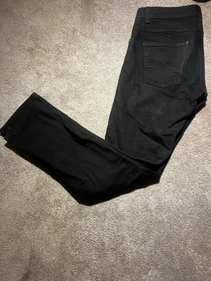  Nudie Jeans - Säljer ett par svarta jeans från Nudie Jeans med klassisk femficksmodell. Jeansen har en stilren look och är tillverkade i ett mjukt, Perfekta för dig som gillar en enkel och clean stil.