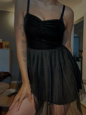 Svart kort klänning med tyllkjol - Säljer en svart kort klänning med smala axelband och figurnära överdel i sammet. Kjolen är i flera lager tyll som ger ett fluffigt och skirt intryck. Gammal design från hm. Storlek S 