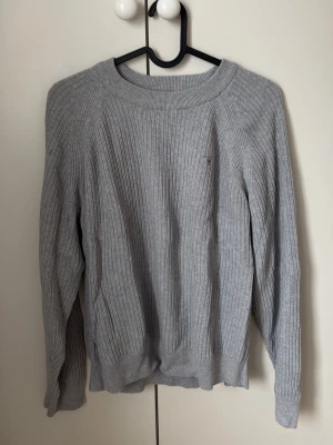 Ljusgrå stickad tröja GANT - Ljusgrå stickad tröja från GANT med diskret logga broderad på bröstet. Tröjan är använd men i väldigt bra skick.