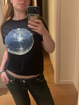 Mörkblå t-shirt med discokula-tryck - Cool mörkblå t-shirt med ett stort discokula-tryck i silver på bröstet. Modellen är croppad och har korta ärmar. Perfekt för dig som vill sticka ut med en unik look