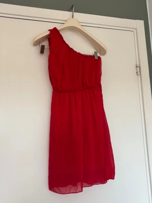 Röd one shoulder kortklänning - Snygg röd kortklänning med one shoulder-design och markerad midja. Har själv köpt den på Plick och vet inte märket tyvärr