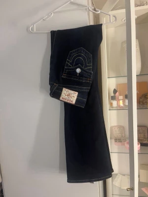 Mörkblå bootcut jeans från Becca - Snygga mörkblå bootcut jeans från Becca med kontrastsömmar och klassisk femficksdesign. Jeansen har en dekorativ ficka med lock och knapp bak samt en mid rise passform. Perfekta för dig som gillar en tidlös och cool look.