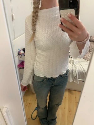 Vit långärmad topp med struktur - Säljer en vit långärmad topp med diskret strukturmönster och lätt utsvängda ärmslut. Toppen har en rund halsringning och sitter figurnära. 
