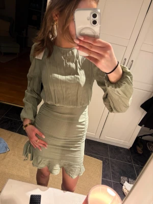 Ljusgrön omlottklänning med volang - Säljer en ljusgrön kortklänning med långärmade puffärmar och omlott-detalj. Klänningen har snörning i sidan och volangkant nedtill. Passar till sommar awn likså till stranden! Perfekt för vår och sommar. Något för dig som vill ha något coolt och snyggt!💕Prislapp kvar och pris kan diskuteras vid snabb affär!