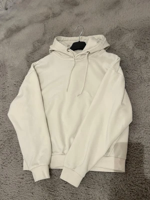 Vit basic hoodie  - En stilren vit hoodie med luva och snörning. Hoodien har ribbade muddar vid ärmslut och midja samt en avslappnad passform. Tillverkad i mjukt bomullsmaterial som känns skönt mot huden. Perfekt för en chill och enkel look. Lite tecken på användning i halsen men inga smink fläckar, annars väldigt bra skick. Använd men inte väl använd. Storlek xs men passar även s. 