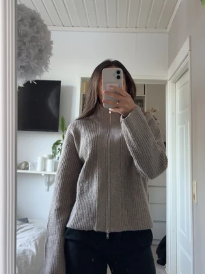 Beige ribbstickad zip-kofta - Jätte fin brun/beige ribbstickad kofta med dragkedja framtill och hög krage. Tröjan är i storlek xs och skulle säga att den är ganska stor i storleken. Jag har enadast använt den 1 gång så den är i mycket bra skick. Inga noppror eller fläckar.