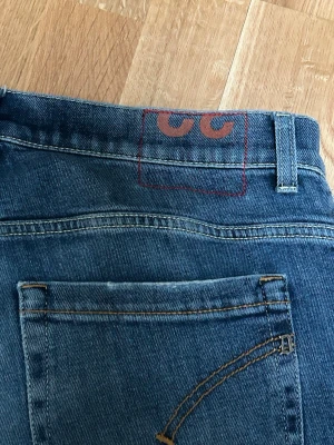 Blå jeans från Dondup. Modell George. W32. - Snygga blå jeans från Dondup, tillverkade i Italien. Klassisk femficksmodell med kontrastsömmar och en unik röd detalj på baksidan vid linningen. Perfekta för dig som gillar stilrena och trendiga jeans i denim. Väldigt bra skick. W32. Nypris 3199kr. Fraktas inom en dag. SKICKA PRISFÖRSLAG OM NI INTE GILLAR PRISET.