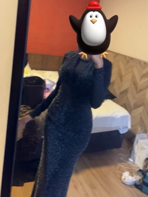 Glittrig långklänning i svart - Snygg svart långklänning med glittrigt tyg och långärmad design. Klänningen har en figurnära passform och passar perfekt när du vill sticka ut. Den har liten slit där bak. Helt oanvänd.