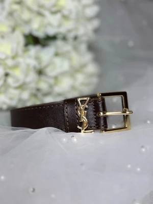 Brunt skärp från Saint Laurent - Snyggt brunt skärp från Saint Laurent med klassiskt YSL-spänne i guld. Bältet är gjort i slätt skinn och har en stilren, fyrkantig guldfärgad metallspänne. Perfekt accessoar för att lyfta vilken outfit som helst.