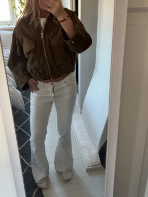 Vita bootcut jeans med hög midja - Säljer ett par vita jeans med bootcut-modell och hög midja. Jeansen har klassisk femficksdesign och stängs med dragkedja och knapp. Snygga att styla med crop tops eller oversized jackor för en trendig look.