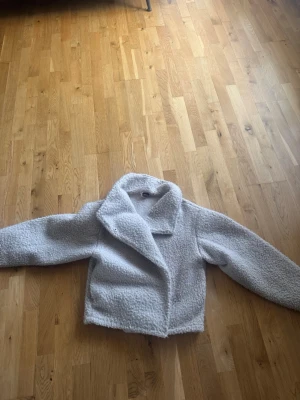 Ljus teddyjacka från Gina Tricot - Supermjuk och fluffig teddyjacka i ljusbeige från Gina Tricot. Jackan har bred krage, rak passform och långa ärmar. Perfekt för att hålla sig varm och snygg under kyliga dagar. Materialet är teddy/fuskpäls som ger en mysig känsla. Säljs ej längre!