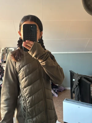 Olivgrön dunväst med dragkedja - Snygg olivgrön dunväst med quiltade paneler och hel dragkedja framtill. Västen har en sportig look och är tillverkad i ett lätt material som passar perfekt för lager-på-lager. Diskreta sidofickor och stilren design utan synligt märke.