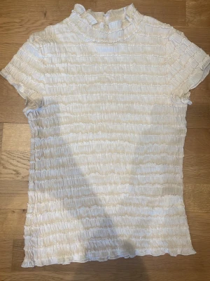 Vit ribbad t-shirt med volangkrage🪩💕 - Säljer en söt vit ribbad t-shirt med korta ärmar och volangdetalj vid halsen. T-shirten har en stretchig struktur och en lätt rynkad look som ger en unik touch till outfiten. Perfekt att styla med kostymbyxor för en trendig vibe. Väldigt bra kvalitet! 🧸🤍🪩