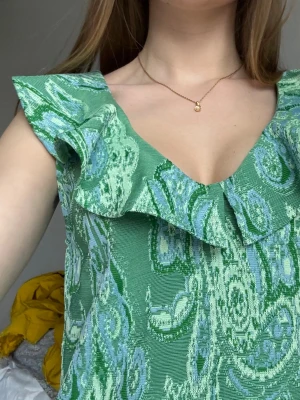Grön volangblus från Zara - Supersöt grön blus från Zara med volangdetalj längs den v-ringade halsen. Toppen har ett mönster i gröna och ljusblå toner och är ärmlös. Står L i lappen (?) Men passar mig som har xs/s
