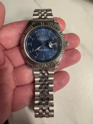 Seiko Mod Datejust blå urtavla stållänk - Supersnygg Seiko Oyster Perpetual Datejust med blå urtavla och datumfönster. Helt ny! Klockan har en klassisk räfflad bezel och robust länkarmband i stål. Perfekt accessoar för dig som gillar tidlös design och exklusiv känsla. Riktigt blank och fräsch!