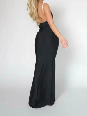 Svart långklänning med pärlband - Elegant svart långklänning med smala axelband dekorerade med pärlor. Klänningen har en figurnära passform och öppen rygg, vilket ger en stilren och sofistikerad look. Klänningen är bara använd en gång.