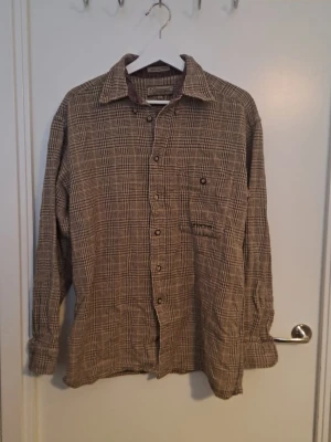 Brun rutig skjorta  - Brun och beige rutig skjorta från Paramount i 100 bomull. Skjortan har klassisk krage, knappstängning framtill och en bröstficka med knapp. Väldigt fin. 🩷