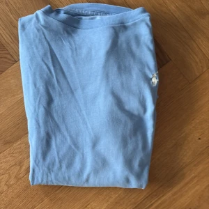 Ljusblå långärmad tröja från Polo Ralph Lauren - Snygg ljusblå långärmad tröja från Polo Ralph Lauren med klassisk rund hals och den ikoniska broderade loggan på bröstet. Mjuk och skön bomull som passar perfekt till jeans eller shorts. Enkel och stilren design som funkar året runt.