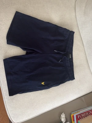 Marinblå shorts från Lyle & Scott - Snygga marinblå shorts från Lyle & Scott med elastisk midja och snörning. Perfekta för sommardagar och avslappnade tillfällen. Tillverkade i mjuk bomull för skön komfort. Skick: 9,5:10😮‍💨🔥🍾👍🏻. Storlek: 12-13 år😮‍💨🤙🏼👍🏻🔥
