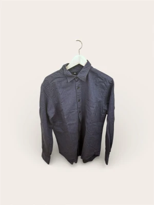 Uniqlo Långärmad Skjorta (Mörkblå) – Stl M - Säljer en klassisk långärmad skjorta från Uniqlo i en stilren mörkblå färg. Ett utmärkt basplagg i garderoben som fungerar både till vardags och till mer uppklädda tillfällen.  Specifikationer:  Märke: Uniqlo  Typ: Långärmad skjorta  Storlek: M  Färg: Blå / Mörkblå  Skick: Fint begagnat skick, dock ostruken på bilden. Hel och ren. Mitt hem är helt djur- och rökfritt.  Finns i Bromma. Snabb och smidig affär prioriteras.