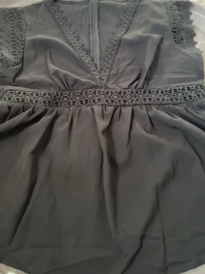 Svart blus med spetsdetaljer - Snygg svart blus med v-ringning och breda spetsdetaljer längs ärmar, midja och halsringning. Blusen har ett löst fall och markerad midja med genombruten spets. Perfekt för dig som gillar romantiska detaljer och en avslappnad men ändå chic look.