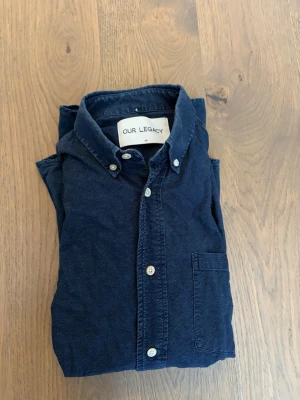 Mörkblå skjorta Our Legacy - Säljer en mörkblå skjorta från Our Legacy i 100% bomull. Skjortan har klassisk button-down krage, bröstficka och vita knappar. 