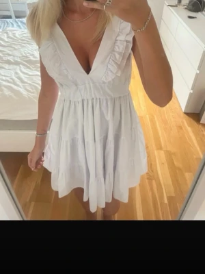 Vit volangklänning med v-ringning - vit kortklänning med v-ringning och volangdetaljer längs axelbanden och urringningen. Klänningen har en luftig passform och är ärmlös, perfekt för skolavslutningen. Storlek xs. Kom tyvärr aldrig till användning så lappen är kvar. Nypris 899