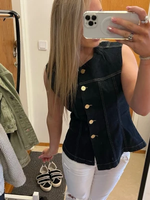 Svart denimväst med guldknappar - Snygg svart väst i denim med markerade sömmar och guldiga knappar framtill. Använd fåtal gånger, säljer då den är för stor för mig.