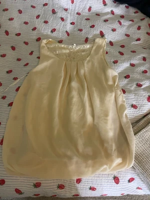 Ljusgul ärmlös topp med spets - Supersöt ljusgul linnetopp och en öppen rygg med spetsinsats. Toppen är ärmlös och är perfekt att styla med jeans eller kjol för en fräsch look.