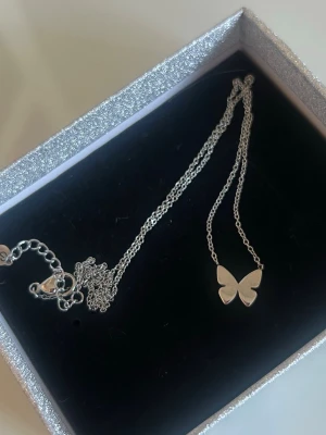 Silverfärgat halsband med fjärilshänge - Snyggt halsband från Edblad i silverfärg med ett stilrent fjärilshänge. Kedjan är tunn och smidig, perfekt för att ge en subtil touch till din outfit. Levereras i kommer i en Edblad ask! Aldrig använt!!