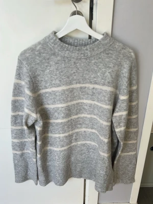 Grå stickad tröja från Vero Moda - Säljer en grå stickad tröja från Vero Moda med vita horisontella ränder💕💕Tröjan har en avslappnad passform, ribbade muddar och rund halsringning💕💕I nytt skick💕💕Jag säljer den 100 kr💕💕Hör av er vid intresse💕💕