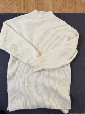 Vit ribbstickad polotröja - Säljer en enkel och stilren vit ribbstickad polotröja med lång ärm. Tröjan har en hög hals och är gjord i mjukt material som känns skönt mot huden. Perfekt att matcha med jeans eller kjol för en clean look.