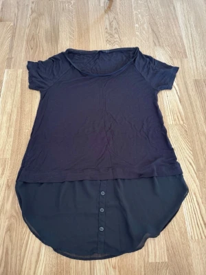 T-shirt Lindex  - T-shirt från Lindex i storlek M. Blusmaterial nedtill.  Fint skick. (Ser missfärgad ut på bilden, men den är ej det i verkligheten, endast så pga ljuset)