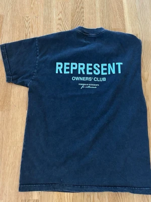 Blå Represent Owners' Club T-shirt - Snygg mörkblå T-shirt från Represent med trycket 'REPRESENT OWNERS' CLUB' i ljusblått på ryggen och mindre logga på bröstet. Klassisk passform med korta ärmar och rund hals. Perfekt för dig som gillar streetwear och vill sticka ut.