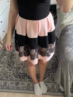 Svart och rosa kort klänning - Söt kort klänning med svart överdel och kjol i rosa och svart med spetsdetaljer och blommigt mönster längst ner. Klänningen har en markerad midja och är ärmlös, perfekt för sommarens tillfällen.