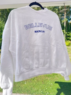 Vit sweatshirt med tryck från Nelly - Vit sweatshirt med blå text broderat på bröstet. Avslappnad passform.  Passar oversized på mig som är storlek S 💞 Säljer pga att den inte kommer till användningen längre. Längd: 58 cm - Axel: 69 cm
