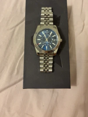 NIBOSI silverfärgad klocka blå urtavla - Stilren klocka från NIBOSI med silverfärgad länk i metall och blå urtavla. Klockan har tydliga vita markeringar, datumvisning och en klassisk rund form. Perfekt accessoar för dig som gillar en modern och elegant look.