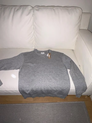 Grå sweatshirt från Jack & Jones - Klassisk grå sweatshirt från Jack & Jones i mjukt ekologiskt bomullsmaterial. Tröjan har rund halsringning, långa ärmar och ribbade muddar vid ärmslut och nederkant. Enkel och stilren design som passar till det mesta.