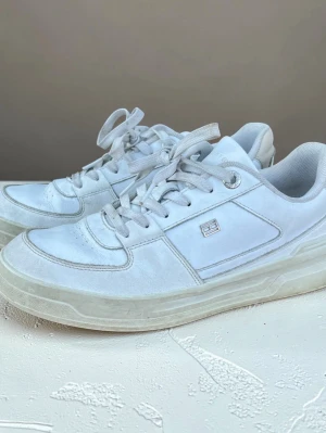 Vita sneakers från Tommy Hilfiger - Stilrena vita sneakers från Tommy Hilfiger. Skorna har ovandel i läder och textil, vita snören och diskret logga på sidan. Perfekta för en clean och enkel look.