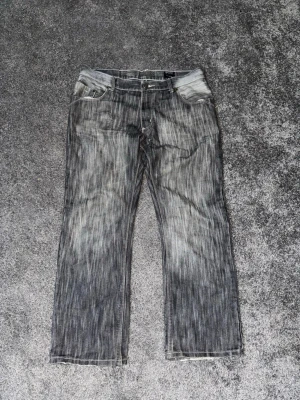 Grå tvättade jeans från Blue Inc - Säljer ett par grå tvättade jeans från Blue Inc med raka ben och klassisk femficksmodell. Baksidan har två fickor, varav en med EDC-broderi. Jeansen har en cool slitningseffekt och är tillverkade i bomull. Perfekta för en avslappnad streetstil.