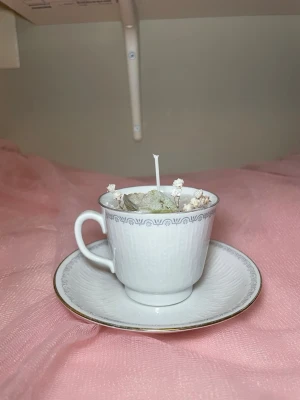 Doftljus i en vaniljdoft i en tekopp med fat med blå design  - Det här ljuset är gjort av återanvändbara material. Tekoppen är köpt secondhand och stearinet är från kyrkor som tänkte slänga det. Det här ljuset har en svag doft utav vanilj, så känsliga även kan använda det. Det här ljuset har även torkade blommor på som dekoration. 