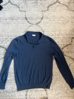 Blå långärmad tröja John Henric - Snygg blå långärmad tröja från John Henric med klassisk krage och två knappar vid halsen. Tröjan har ribbade muddar vid ärmslut och nederkant. Perfekt för dig som gillar stilrena och enkla plagg.