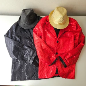 Glittrig paljettkavaj röd & svart + svart och guldig hatt - Två kavajer i syntetmaterial, en röd och en svart, båda täckta med glittriga paljetter. Klassisk kavajmodell med knappar framtill och lång ärm. Perfekt för dig som vill sticka ut med en färgstark och glittrig look.