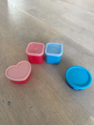 Små färgglada plastburkar - Fyra små plastburkar i olika former och färger: en hjärtformad rosa, en rund blå samt två fyrkantiga i rosa och blått. Perfekta för snacks, såser eller till pysselförvaring. Alla burkar har tillhörande lock och är tillverkade i plast.🩷